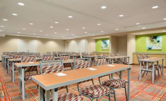 a conference room with rows of tables and chairs , a large screen on the wall , and a green display at Home2 Suites by Hilton Middletown