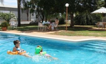 a group of people , including children , are enjoying a day at the pool , playing in the water , with one person swimming and another swimming at Copper City Motel