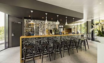 a modern restaurant with a long bar , black chairs , and various food items on display at Ibis Baden Neuenhof