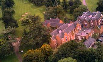 aerial view of a large building surrounded by green trees and grass , with a golf course in the background at Coulsdon Manor Hotel and Golf Club