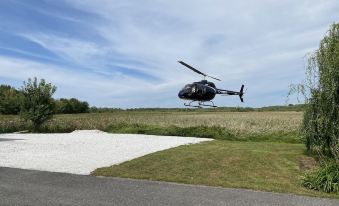 a black helicopter is flying over a grassy field with a white sand runway in the foreground at Château Venise