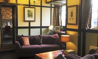 a living room with yellow walls , black furniture , and various paintings on the walls , including one hanging above the couch at The Border Hotel