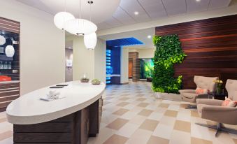 a modern reception area with a white marble counter , green plants , and a checkered floor at Even Hotel Rockville - Washington DC Area