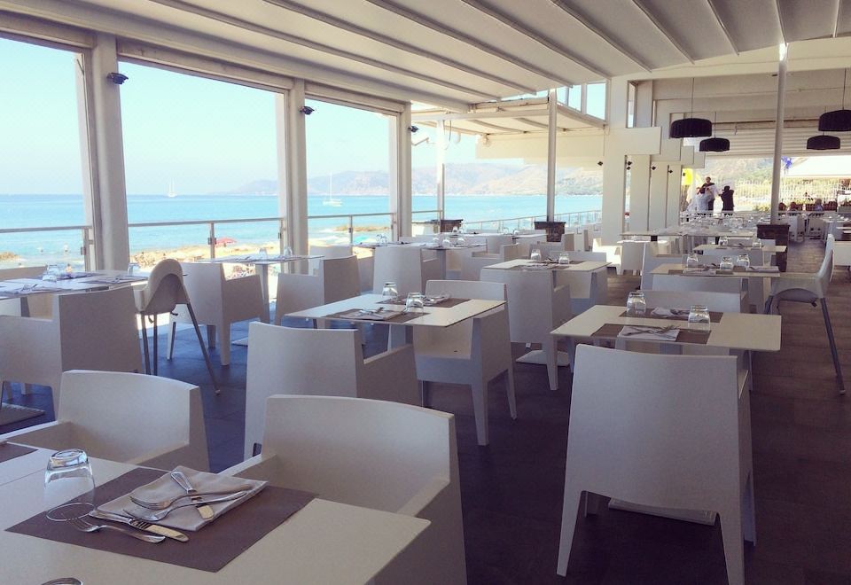 a restaurant with white tables and chairs , large windows overlooking the ocean , and a blue sky at Hotel la Playa