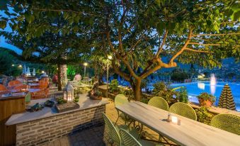 an outdoor dining area with a table , chairs , and a pool in the background at night at Koukounaria Hotel & Suites
