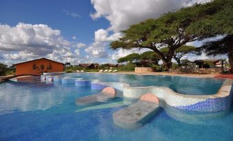 a large outdoor swimming pool surrounded by grass , trees , and buildings , creating a relaxing atmosphere at Kilima Safari Camp