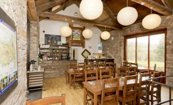 a cozy restaurant with wooden furniture , large windows , and hanging lights , providing a comfortable atmosphere for diners at YHA Brecon Beacons Danywenallt
