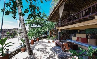 a beach house with a wooden deck and tropical plants , surrounded by palm trees and mountains at La Luz Beach Resort