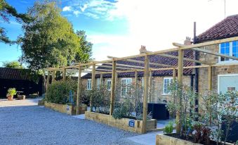 a wooden pergola with plants and trees in front of a house , under a blue sky with clouds at The Durham Ox