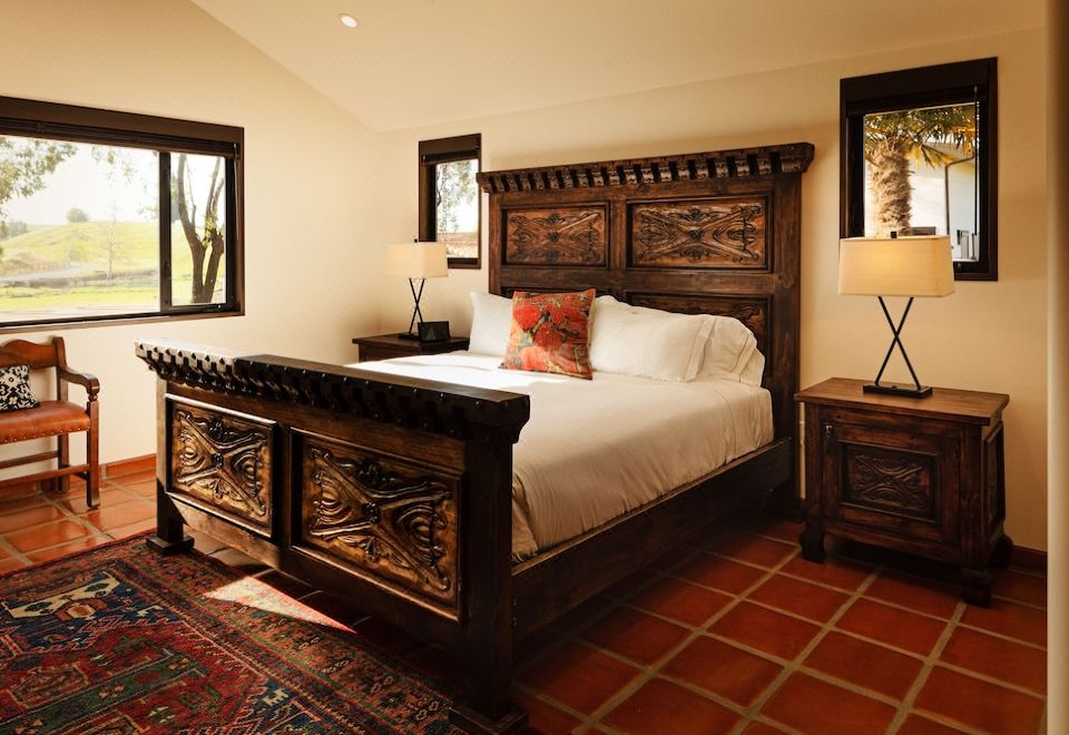 a large bed with a wooden headboard and white linens is in a room with red tile flooring at La Lomita Ranch