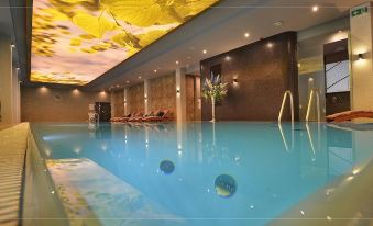 a large indoor swimming pool surrounded by lounge chairs and a ceiling with yellow leaves at Hotel Pod Lipou Resort