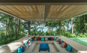 a modern outdoor living area with wooden ceiling , blue lounge chairs , and a blue table surrounded by lush greenery at Island Escape Burasari