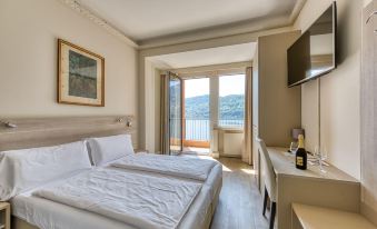 a hotel room with a large bed , a tv , and a door leading to a balcony overlooking a body of water at Hotel Bazzoni