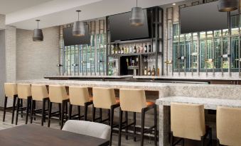 a modern bar with a marble counter , wooden chairs , and several televisions mounted on the wall at Hilton Garden Inn Columbia Airport