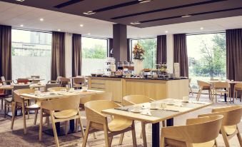 a restaurant with wooden tables and chairs , a counter , and a breakfast area in the background at Hotel Mercure Gdynia Centrum