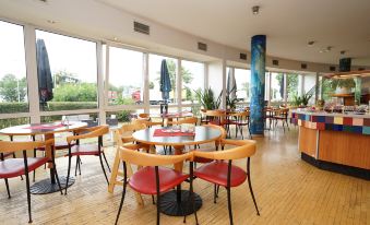 a large dining area with wooden tables and chairs , surrounded by windows that provide a view of the outdoors at Highway Hotel