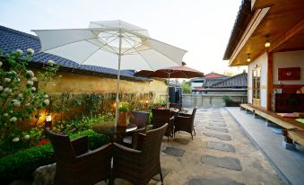 There is a patio on the sidewalk with tables and chairs under an umbrella at Jeonju Dwaejikkum Hanok