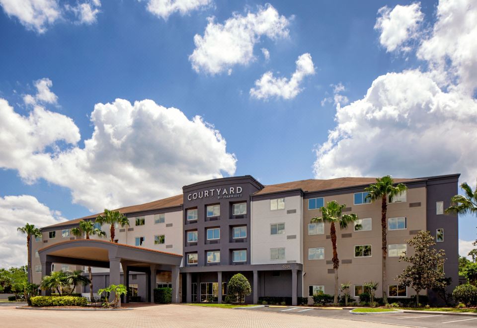 a large building with a courtyard hotel sign , surrounded by palm trees and under a blue sky at Courtyard Tampa Oldsmar