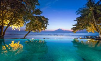 a tranquil scene with a large swimming pool surrounded by trees , reflecting the night sky and the ocean at Jeeva Klui Resort