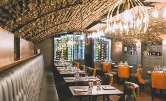 a restaurant with a stone ceiling , multiple dining tables , and orange chairs , illuminated by hanging lights at The Bear, Cowbridge