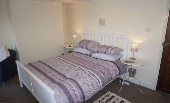a neatly made bed with a white headboard and purple bedding is shown in a bedroom at The Shepherds Inn