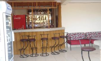 a bar with multiple stools and a red couch , surrounded by bottles on the counter at Coronation Hotel