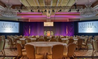 a large room with tables and chairs set up for a meeting or event , featuring purple curtains and stage lighting at Little America Hotel & Resort Cheyenne