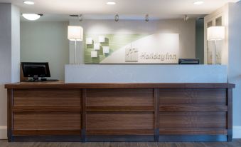 a hotel lobby with a reception desk , a computer , and a vase of flowers on the counter at Holiday Inn South Kingstown (Newport Area)