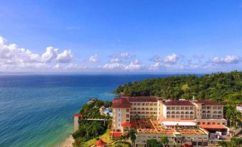 a beautiful beachfront resort with multiple buildings , clear blue skies , and green trees , set against the backdrop of a mountainous landscape at Bahia Principe Grand Cayacoa