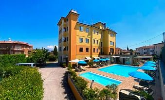 a large yellow building with a swimming pool in front of it , surrounded by grass and trees at Green Park Hotel