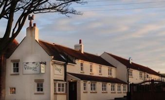 a traditional english village with white buildings and a red roof , set against the backdrop of trees and sky at The Village Inn