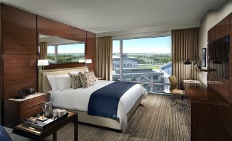 a large bed with a blue blanket is in a room with a window and desk at Omni Frisco-Dallas Hotel at the Star