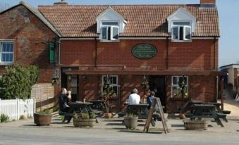 a brick building with a green sign above the entrance , surrounded by several people sitting outside on benches at The Foxham