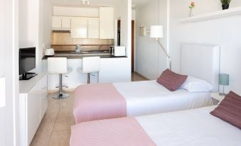 a bedroom with two twin beds and a kitchenette in the background , all decorated in white and pink at Club Olympus in Garden City