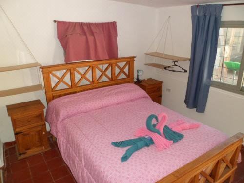 a bedroom with a wooden bed , pink sheets , and a pair of pink towels on it at Alquimia