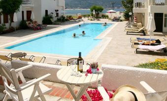 a pool area with lounge chairs , a table , and people enjoying the view of the ocean at Skopelos Village Hotel