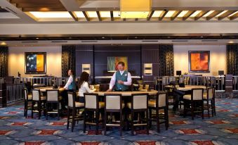 a waiter is standing behind a counter in a restaurant with large tables and chairs at Pala Casino Spa and Resort