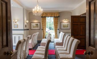 a room with rows of white chairs arranged in a semicircle , facing a window and a chandelier hanging from the ceiling at Woodland Manor Hotel
