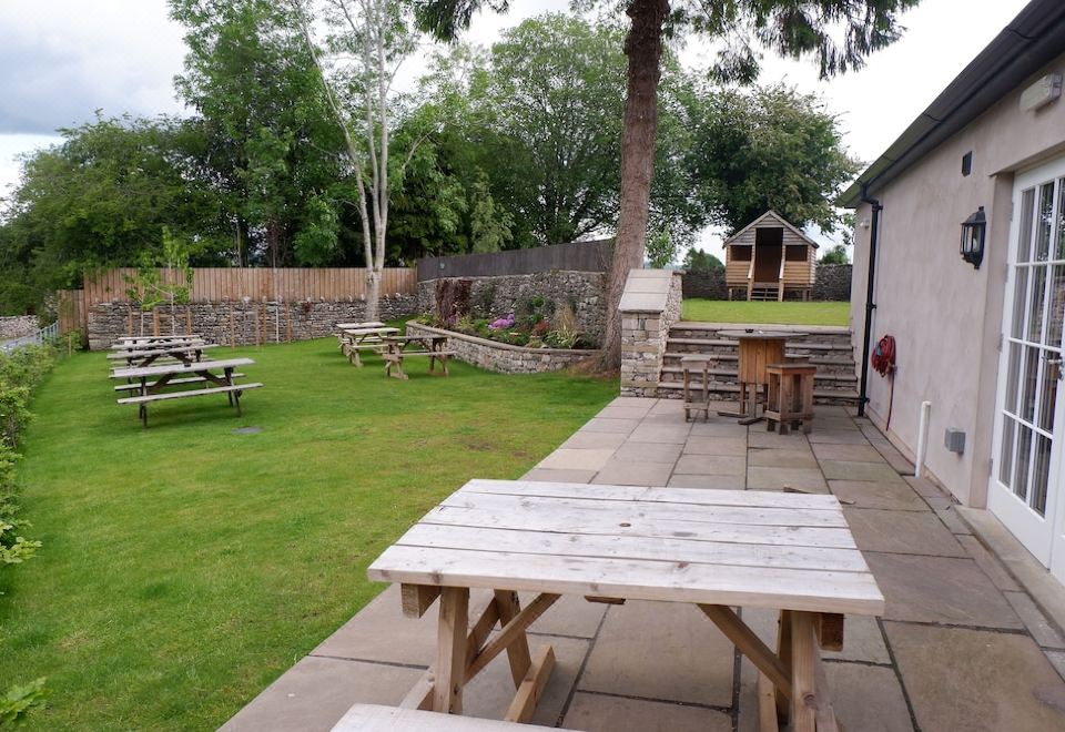 a wooden picnic table is situated in a grassy backyard with benches and a brick wall at The New Inn - Yealand