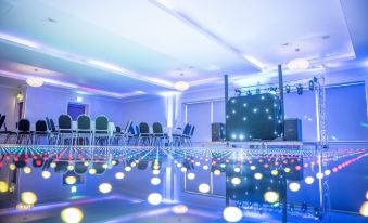 a well - lit room with a stage and numerous lights , including spotlights and microphones , reflecting in the water at Dean Park Hotel