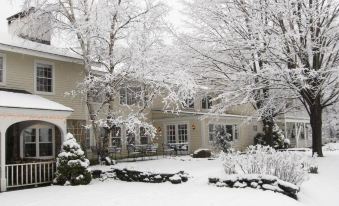 a snow - covered courtyard with a large house and trees covered in snow , creating a picturesque scene at Deerhill Inn