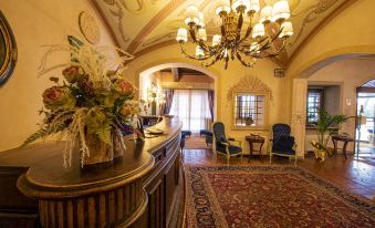 a hotel lobby with a reception desk , chairs , and a rug , decorated with flowers and chandeliers at Hotel Boccaccio