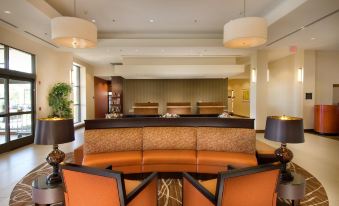 a modern hotel lobby with orange chairs , a marble reception desk , and large windows , creating an inviting atmosphere at DoubleTree by Hilton Dulles Airport - Sterling
