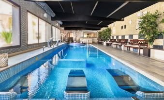 an indoor swimming pool with a modern design , surrounded by comfortable seating and greenery , under a black ceiling at Salles Hotel Aeroport de Girona
