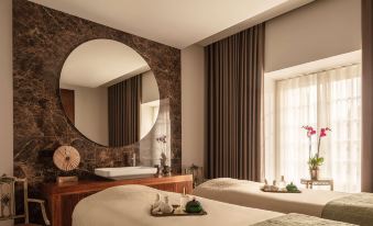 a luxurious spa room with two massage tables , a large round mirror , and towels on the windowsill at Valverde Sintra Palacio de Seteais
