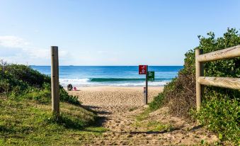 a sandy beach with a path leading to the ocean , where a person is sitting on a chair at Sage Hotel Wollongong