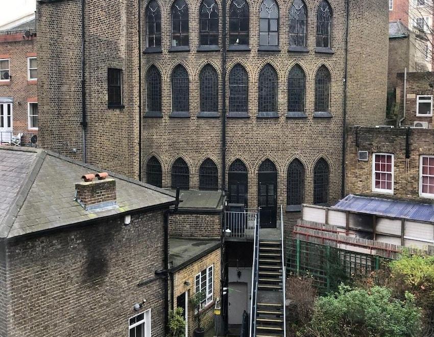 a brick building with arched windows and a staircase leading up to it , surrounded by other buildings at Berjaya Eden Park London Hotel