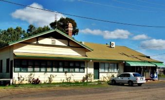a house with a green roof and white walls is surrounded by bushes and trees at Gowrie Hotel Motor Inn