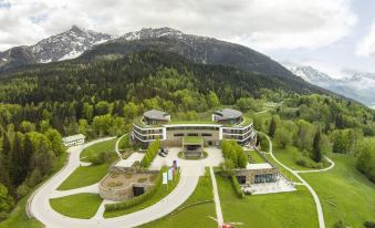 aerial view of a large building surrounded by green grass and mountains in the background at Kempinski Hotel Berchtesgaden