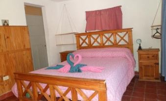 a bedroom with a wooden bed , pink sheets , and a flamingo decoration on the bed at Alquimia